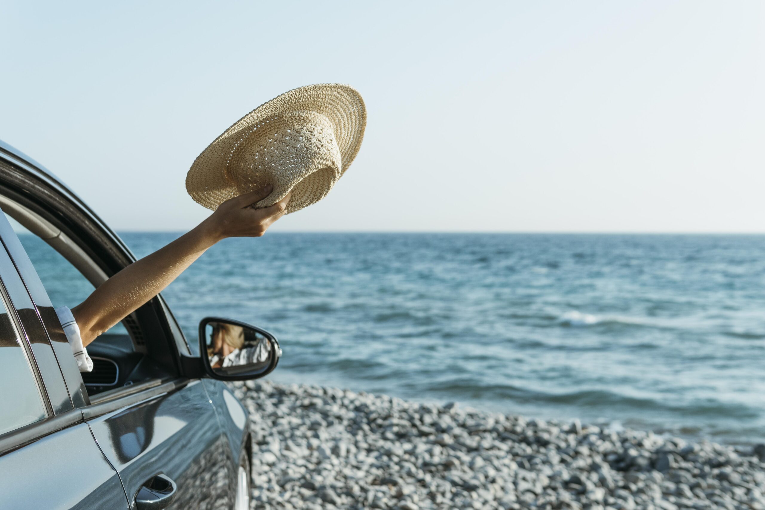 Macchina in spiaggia con braccio fori dal finestrino e cappello estate in vacanza sicilia
